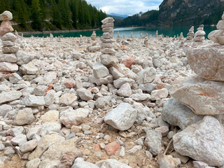 Tourists piling stones one on top of the other, Lago di Braies, Pragser Wildsee in the Dolomites. A view of the entire green-blue lake with the mountain peak in the background.
