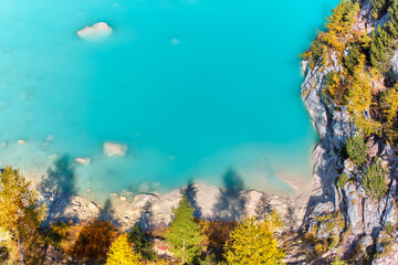 Fototapeta na wymiar Vertical view of Azure water of Lake Sorapiss and coastal beach. Dolomites in autumn. Sunny day, contrast of colors, azure with orange. 