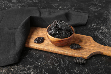 Bowl with tasty prunes and cutting board on black grunge table