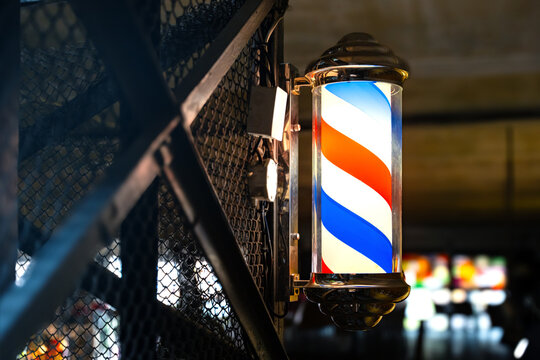 Barber pole of barbershop on vintage industrial wall in the evening. Classic barbershop spinning cylinder to attract customers.