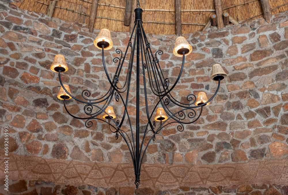 Wall mural forged iron chandelier in a room with stone walls and thatched roof, vintage style