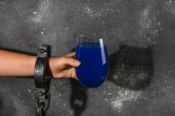 Female hand in shackles holding cocktail on black grunge background. Halloween concept