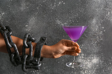 Female hand in shackles holding cocktail on black grunge background. Halloween concept
