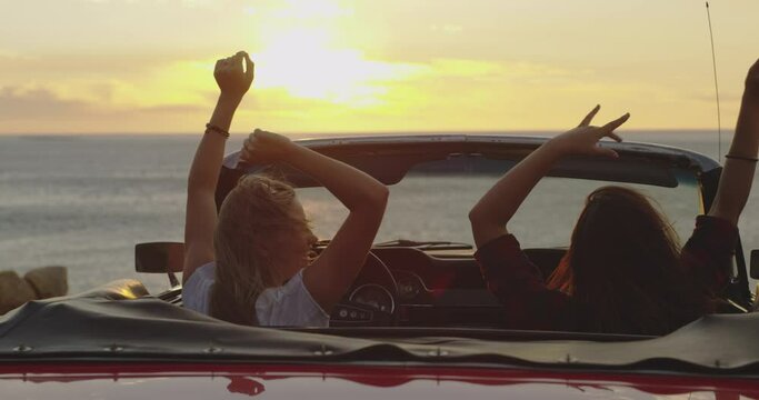 Sunset, dance and girl friends on road trip for holiday, vacation or weekend together. Happy, freedom and back of young women driving a car in wind for transportation, tourism or sightseeing by coast
