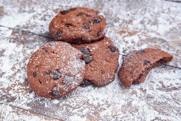 Shortbread cookies with chocolate chips on wooden background sprinkled with powdered sugar. Fresh pastry.