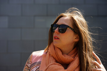 Portrait of mid 30 business woman with brown hair with black sunglasses smiling and gray background.