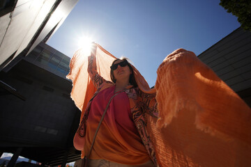 Successful positive woman in orange fashion clothes waving orange scarf in business building...