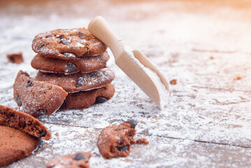 Cookies with chocolate slices sprinkled with powdered sugar and a wooden measuring spoon. Fresh pastry on wooden background.
