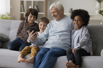 Elderly great-grandfather and three little great-grandchildren having fun with smart phone watch...