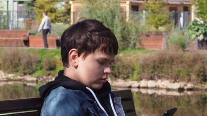 Fototapeta premium smiling happy fun teenage schoolboy boy sits in a park on a bench use mobile cell phone chat online rest relax outdoors Urban. spending time on social networks, online training, conference. video call
