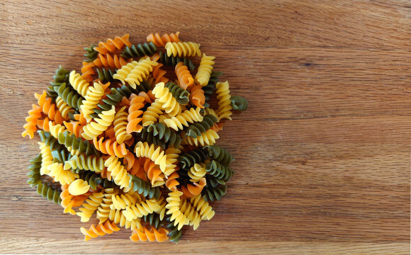 Tri-color rotini corkscrew-like dry pasta on a wood cutting board