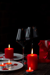 Saint Valentine's Day celebration. Red burning candles, hearts, gift box, postcard on dark wooden background. Happy holiday . Table decor for festive dinner, romantic atmosphere. Copy space for text