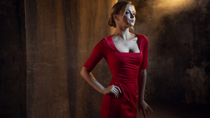 A femme fatale in a red dress. Attractive blonde in an elegant dress with a neckline, sexy and feminine image. photo in dark colors on a textured wall, warm light