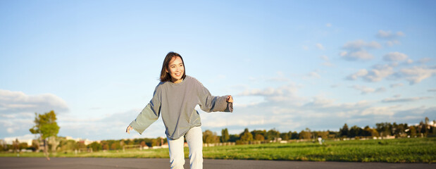 Cute asian girl riding skateboard, skating on road and smiling. Skater on cruiser longboard...