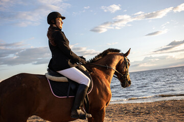 Horsewoman in equestrian sports gear, riding a horse, on the beach, portrait on the background of...