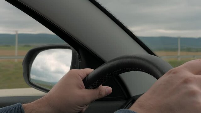 Man drives modern car holding steering wheel along rural road closeup
