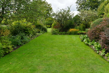 Scenic view of a beautiful garden with a green grass lawn, leafy plants and flowers in bloom