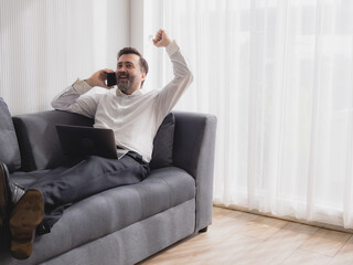 Portrait caucasian senior business man handsome one person smile happy sitting sofa and laptop talking mobile phone plan job work new project along with looking success future in living room office