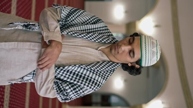 Close-up portrait of an Arab guy in national clothes who prays in the hall of mosque with his eyes closed