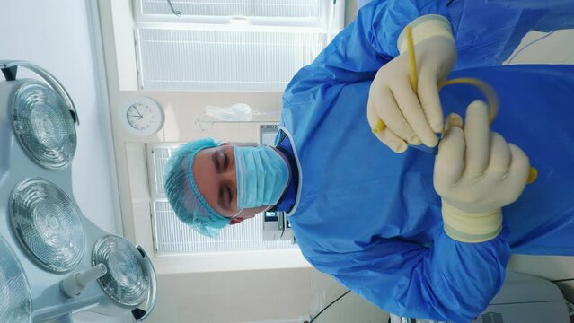Male surgeon in cap, mask and uniform attaches rubber tube to a syringe. Preparation for endosurgery. Vertical screen.