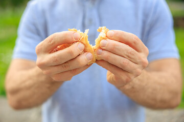 A man's hand breaks a croissant, snack and fast food concept. Selective focus on hands with blurred background