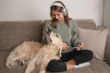 Girl sitting with her dog on the couch with headphones on. Young woman stroking her dog at home.