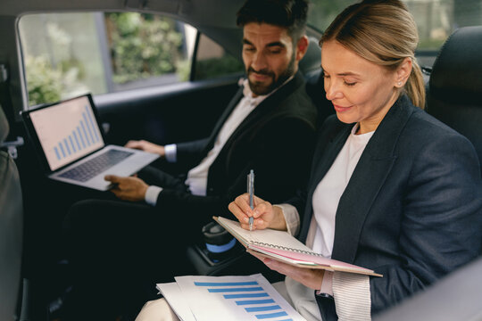 Business Colleagues Working On Laptop While Sitting In Car Backseats. High Quality Photo