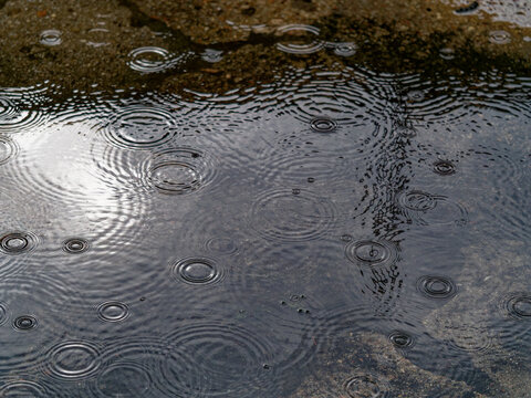 Raindrops falling into small puddle on the sidewalk on rainy day