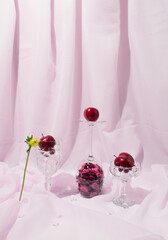 Still life arrangement of cristal glasses filled with red plums against light violet background.