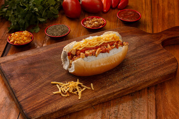 Traditional Brazilian hot dog on top of a wooden board with some ingredients around it.