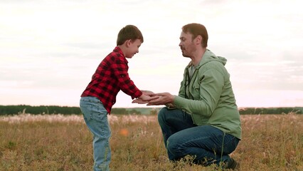 Naklejka na ściany i meble Positive boy gives high-five to father playing in middle of field in agricultural area