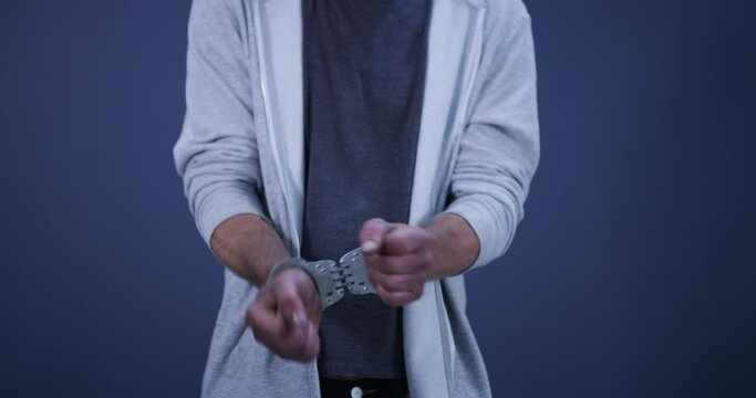 Hands, cuffs and closeup of man criminal in studio for illegal crime, danger or corruption. Arrest, surrender and zoom of male prisoner or suspect in jail for theft, scam or fraud by blue background.