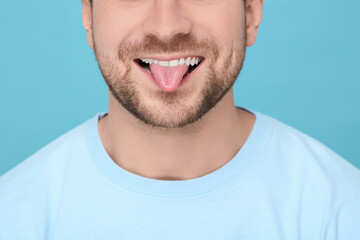Obraz premium Man showing his tongue on light blue background, closeup