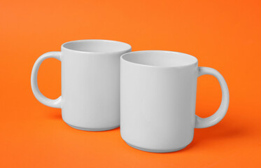 Two white ceramic mugs on orange background