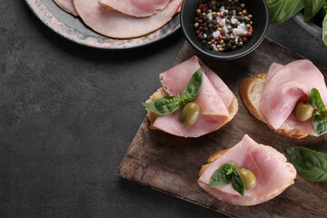 Delicious sandwiches with ham, basil, olives and spices on grey table, flat lay. Space for text