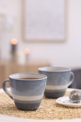 Cups of drink and snap infuser with dry leaves on table indoors, space for text
