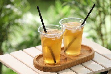 Plastic cups of tasty iced tea with lemon on white wooden table against blurred background