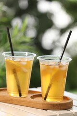 Plastic cups of tasty iced tea with lemon on white wooden table against blurred background