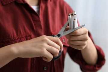 Stop smoking concept. Woman cutting cigarettes on light background, closeup