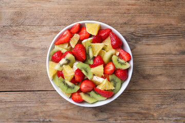 Delicious fresh fruit salad in bowl on wooden table, top view