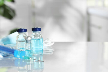 Glass vials, syringe and medical masks on white table. Space for text