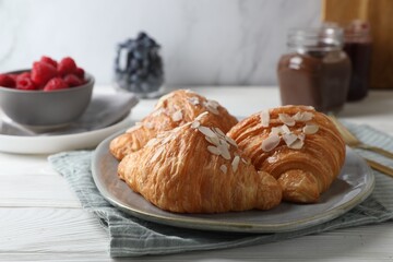 Delicious croissants with almond flakes on white wooden table, closeup