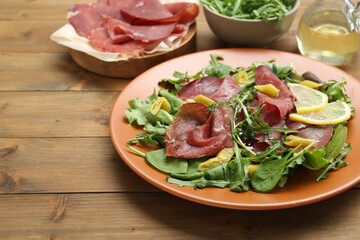 Delicious bresaola salad on wooden table, closeup. Space for text