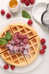 Tasty Belgian waffle with fresh raspberries, honey and powdered sugar on white table, flat lay