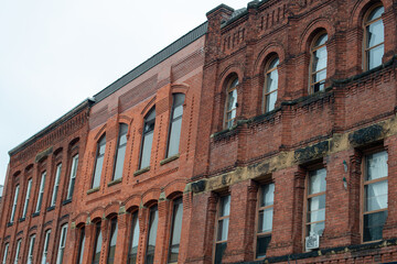 The exterior of multiple brown brick buildings with tall arched glass windows. The classic apartment buildings are adjoined with flat rooftops. The vintage structures have various shades of brick. 