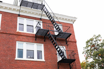 fire escape staircase zigzags outside a brick building, representing escape routes, emergency...