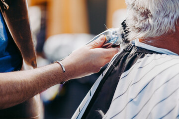 A stylist uses electric clippers to trim and style a clients white hair - obrazy, fototapety, plakaty