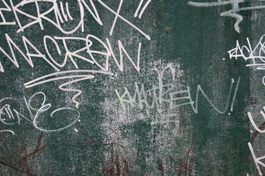 Parede met&aacute;lica verde com grafites e escritas por ela.