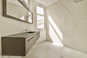 a bathroom with white tile and wood cabinetd vanity in the corner, looking out to the outside through the window