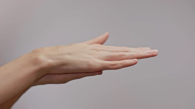 Woman hands spread the cream over her palm towards her hand. Well-groomed hands, natural short nails, on a light background.